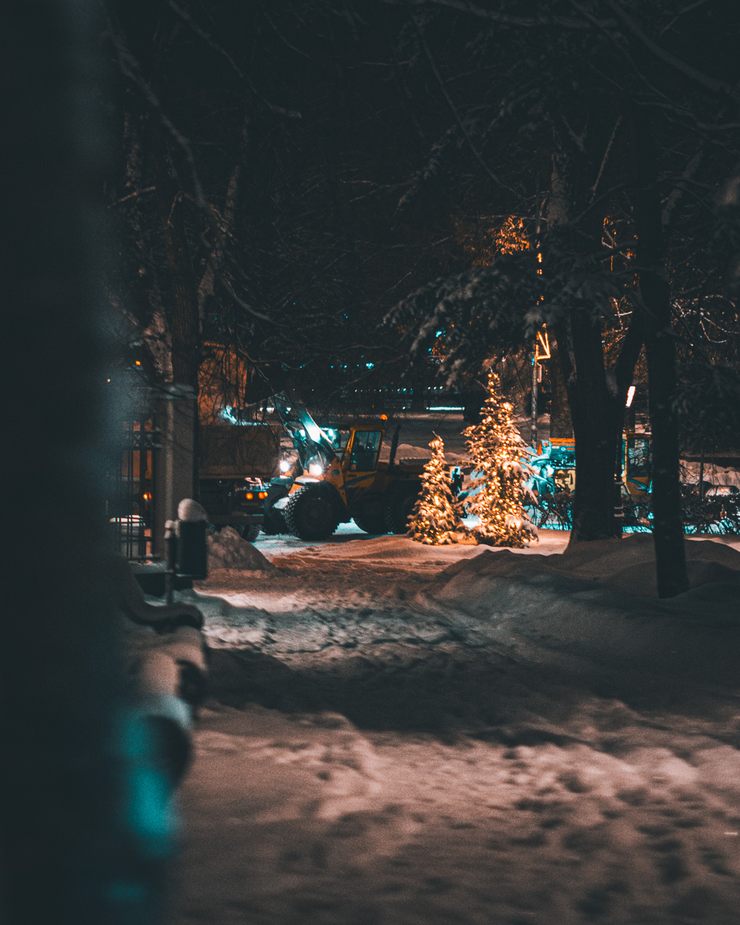 Excavator moving snow on a dark road between trees