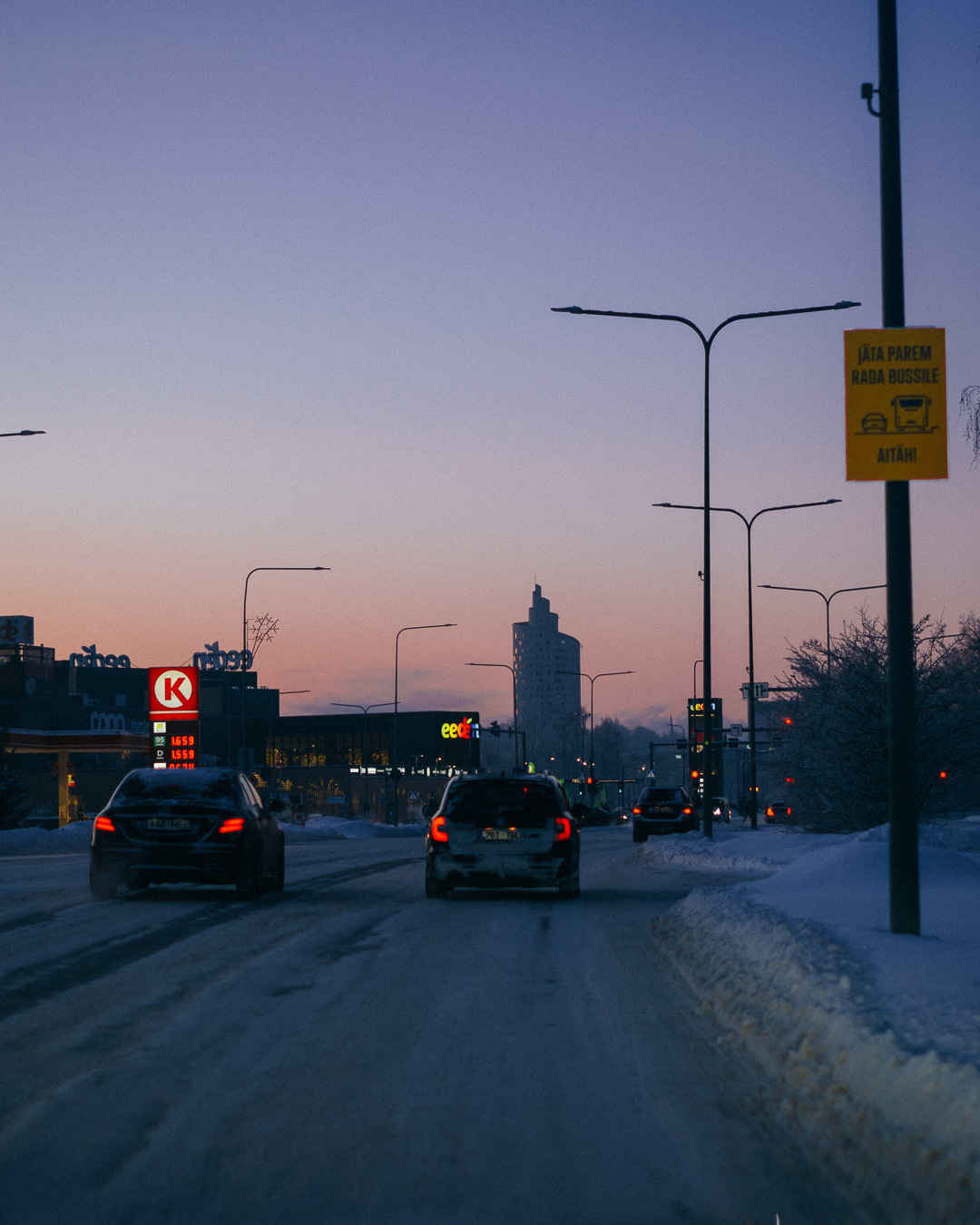 Cars driving on a snowy road with the sunset in the background